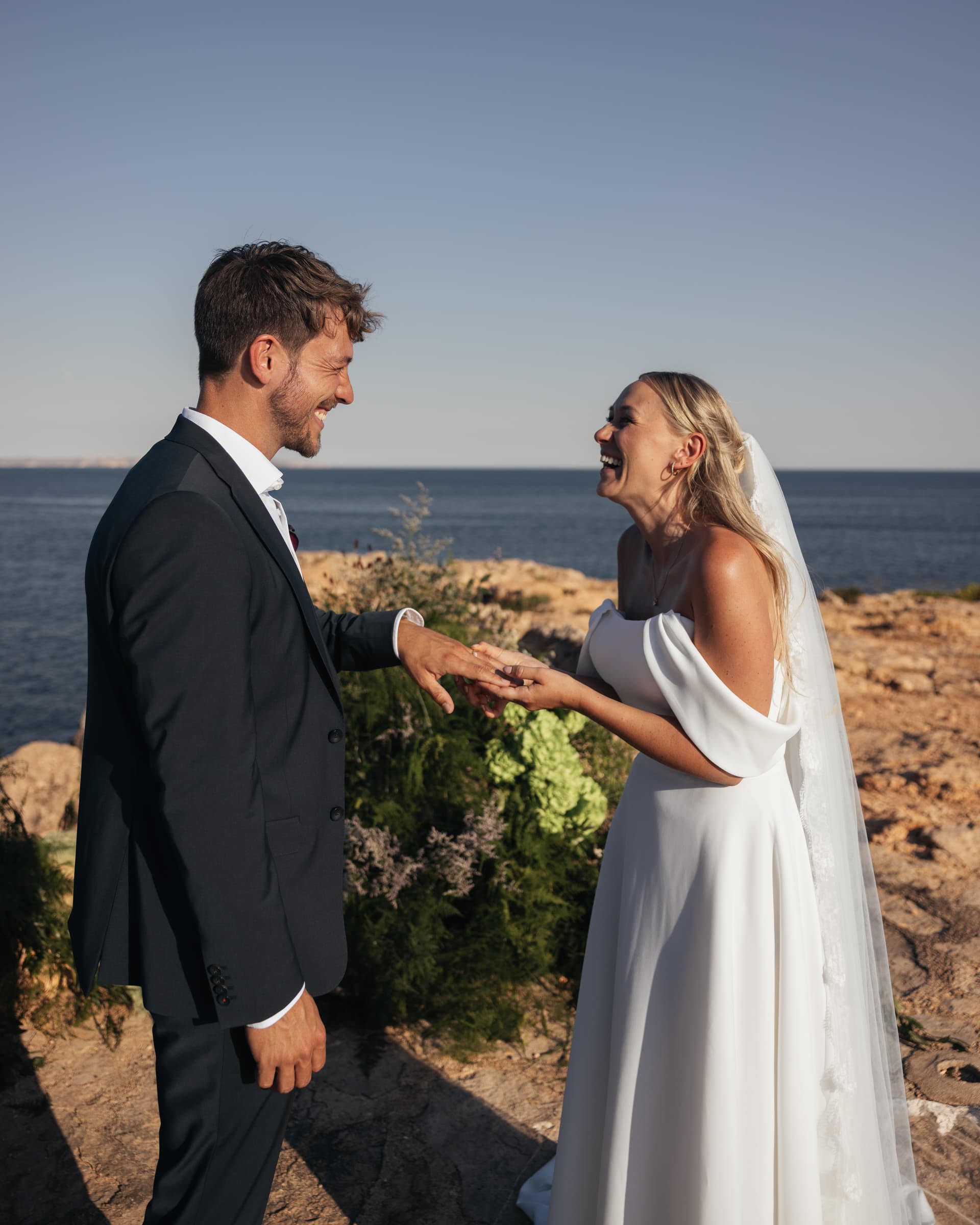 A couple in wedding attire holding hands at the coast.