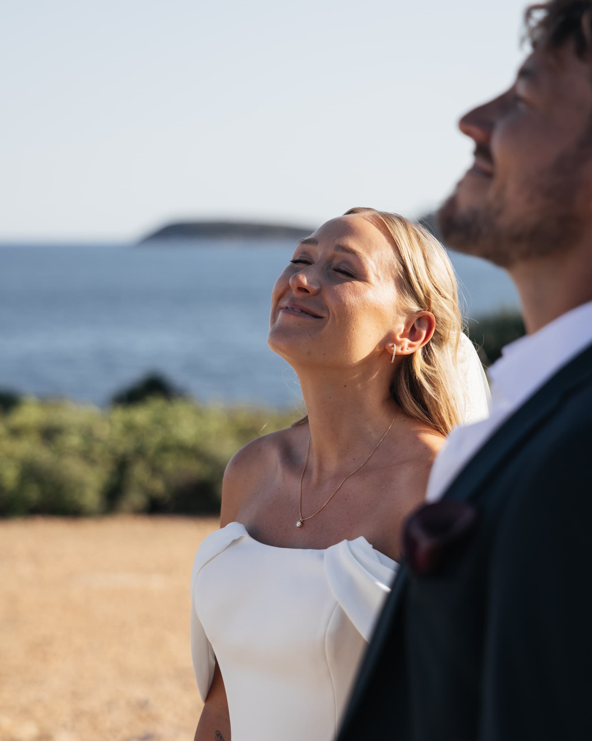 Seitenporträt einer Person im weißen Hochzeitskleid vor dem Meer.