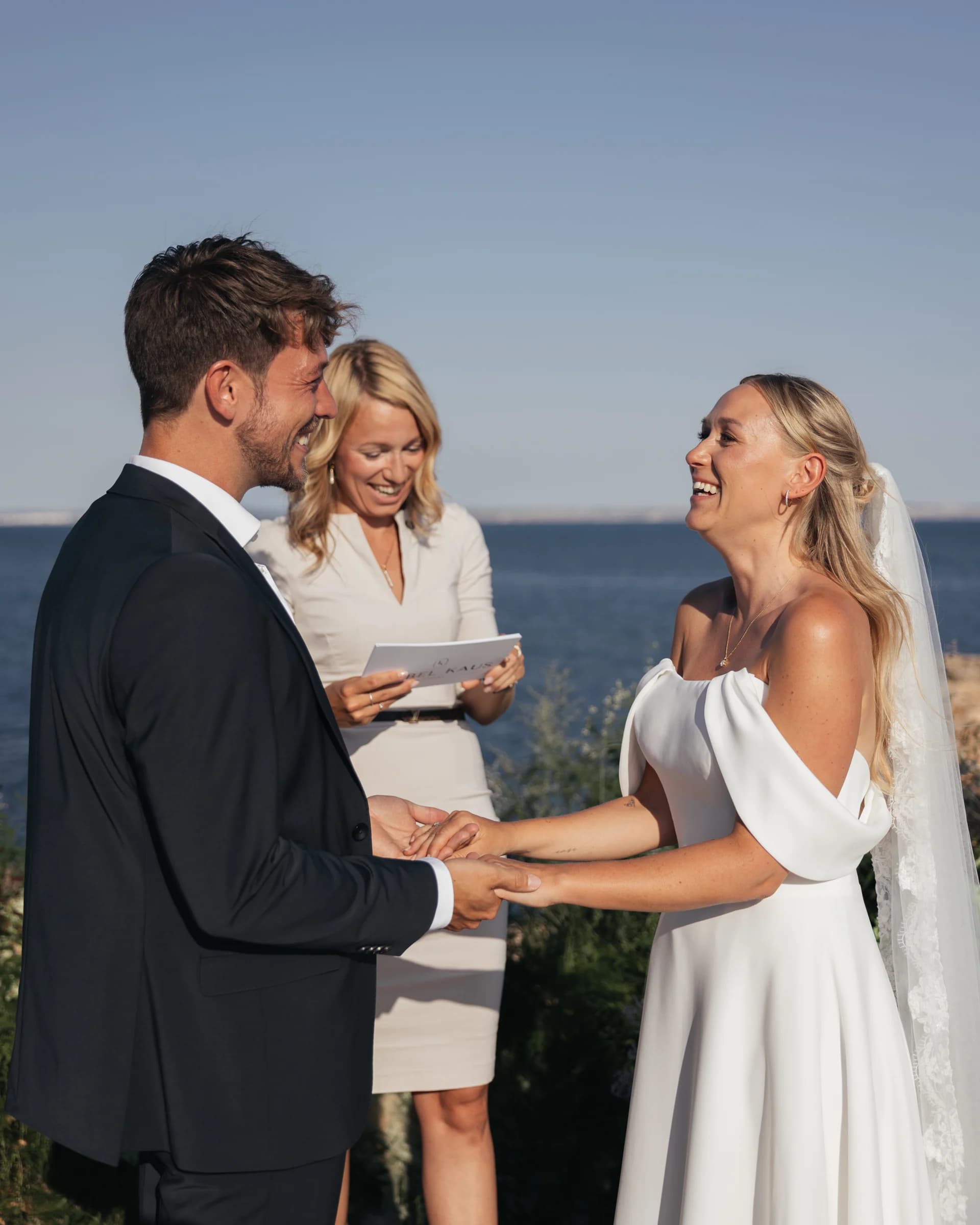 A couple in wedding attire standing with a woman outdoors.