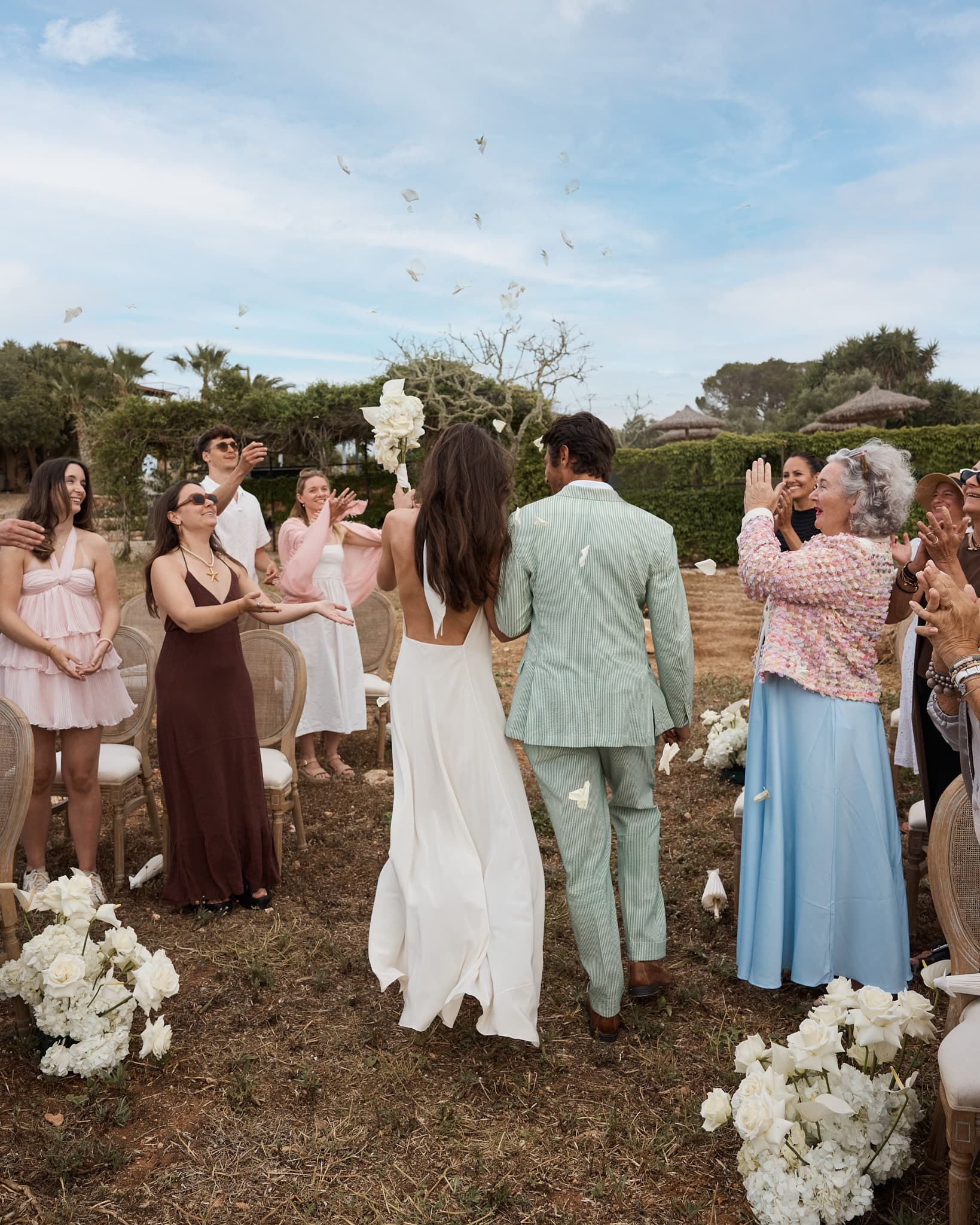 A couple in wedding attire walking between guests outdoors.