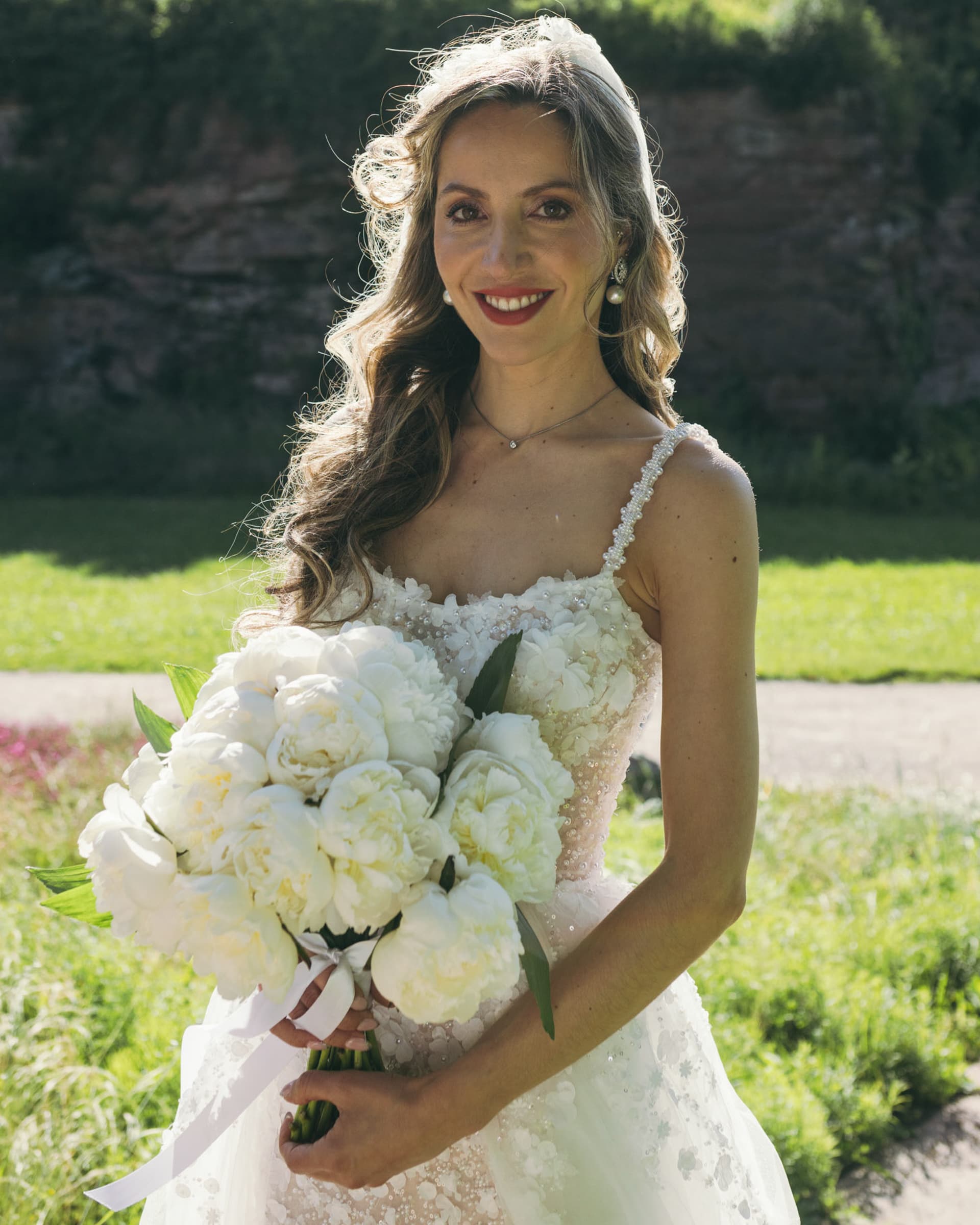 A person in a white wedding dress holding a bouquet outdoors.