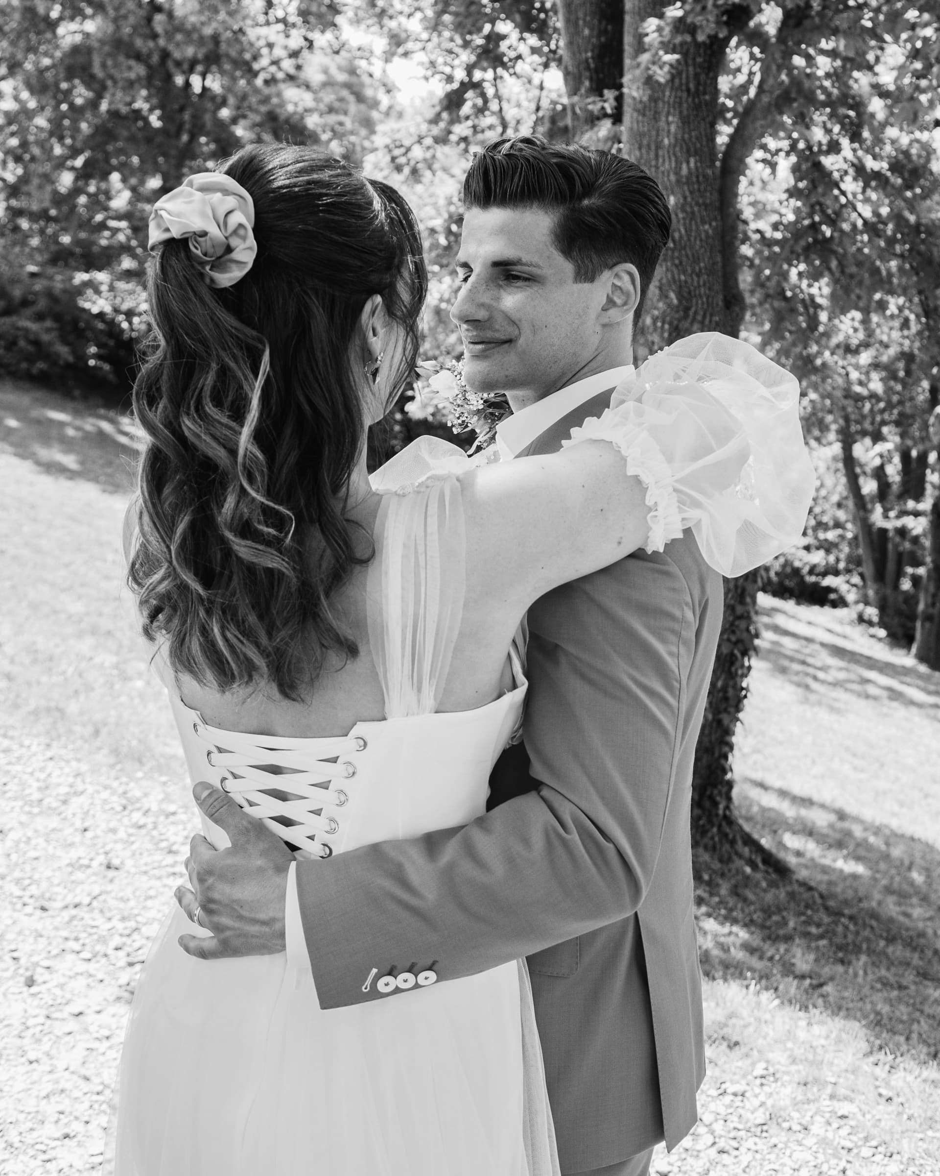 Black-and-white close portrait of a couple in wedding attire outdoors.